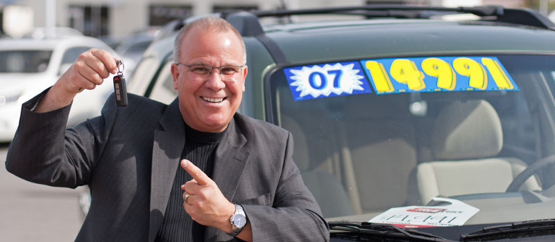 Photo of car salesman smiling and pointing to the keys of certified pre-owned cars.